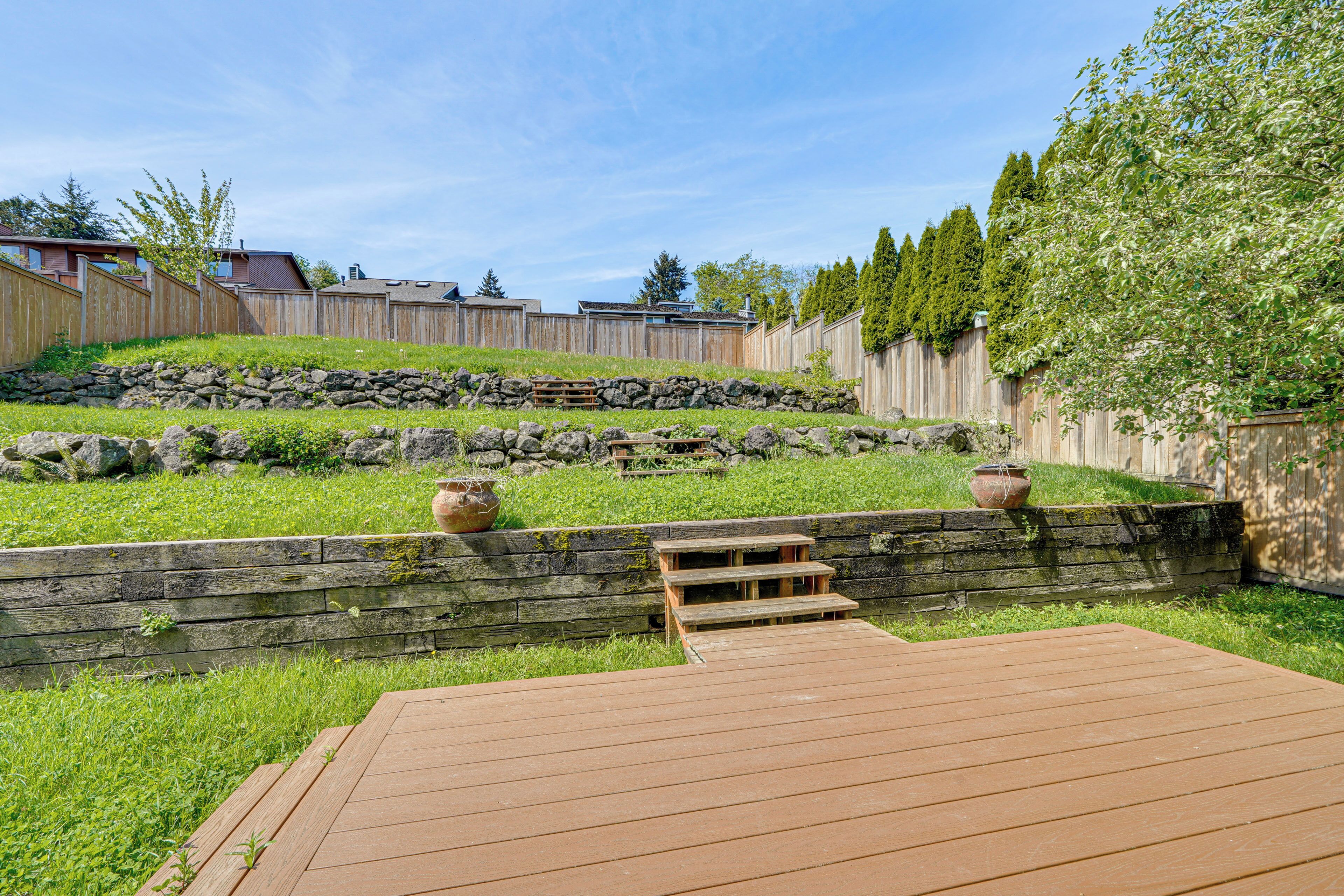 A backyard with a wooden deck, stone wall, and a wooden fence.