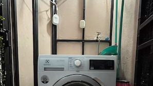 Una lavadora compacta en un lavadero pequeño, con piso de baldosas, un grifo de agua y un enchufe.