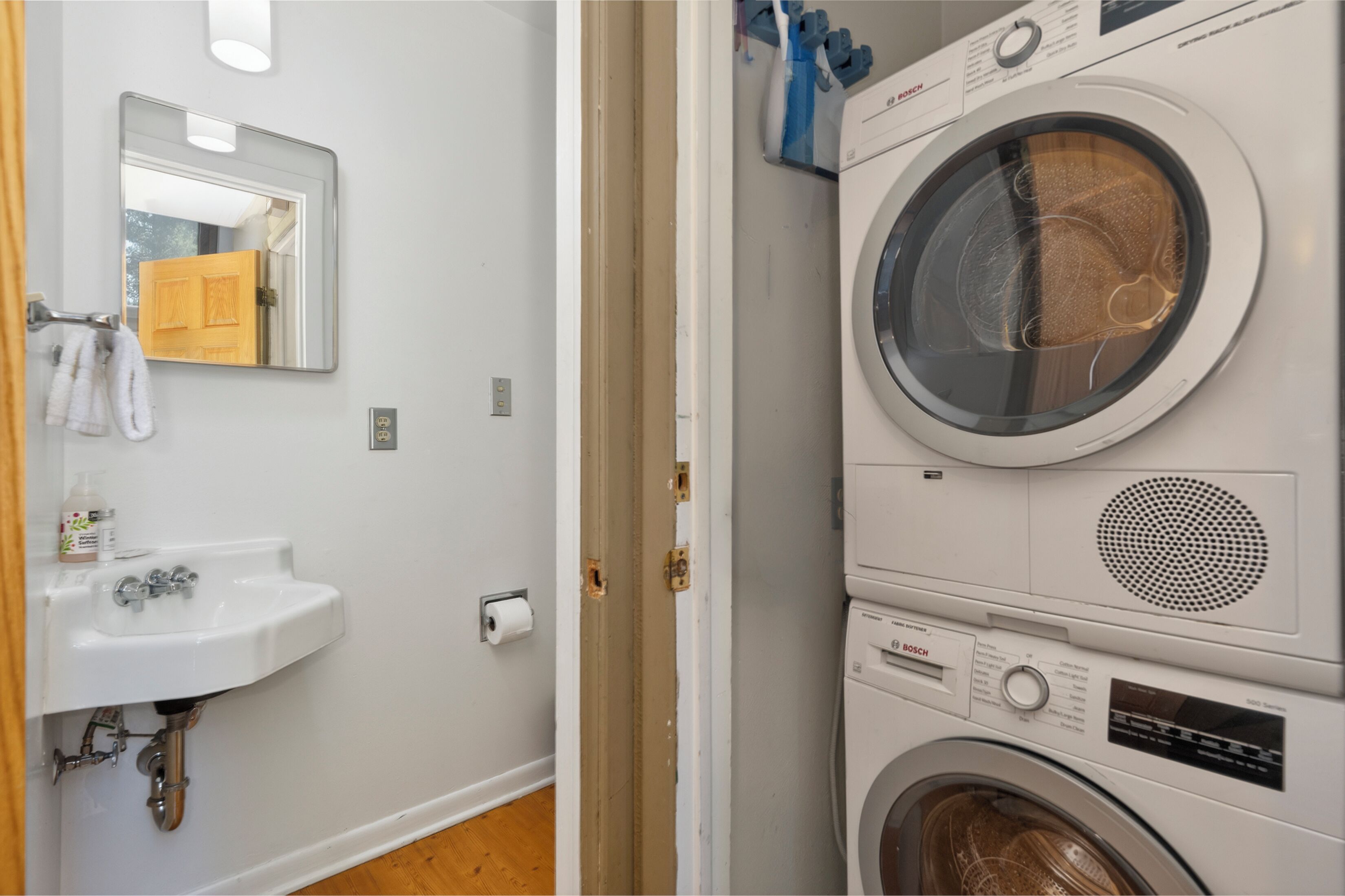Une buanderie équipée d’un lave-linge Bosch, d’un évier avec un savon et d’un miroir qui reflète la pièce.