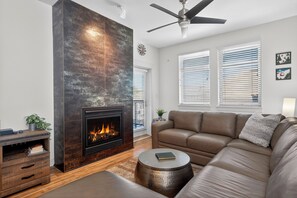 Ein modernes Wohnzimmer mit Kamin, Ledersofa und Deckenventilator.