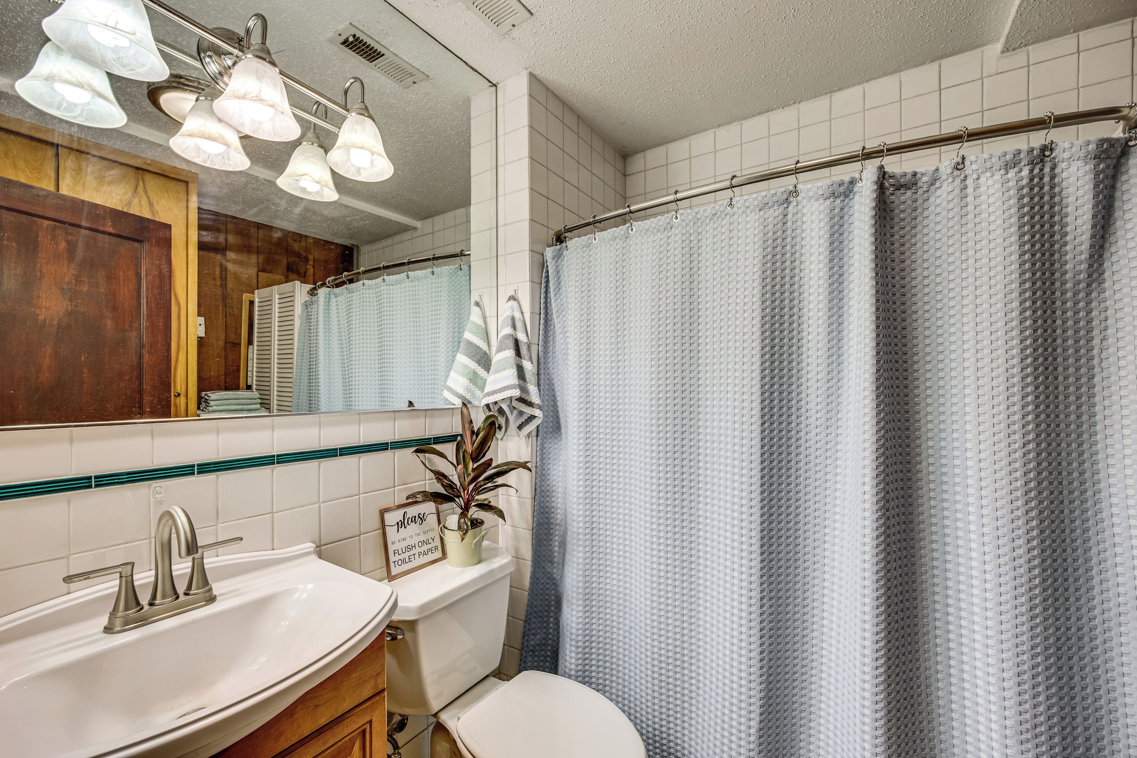 Ein Badezimmer mit weißem Waschbecken, Toilette, Duschvorhang und Spiegel.