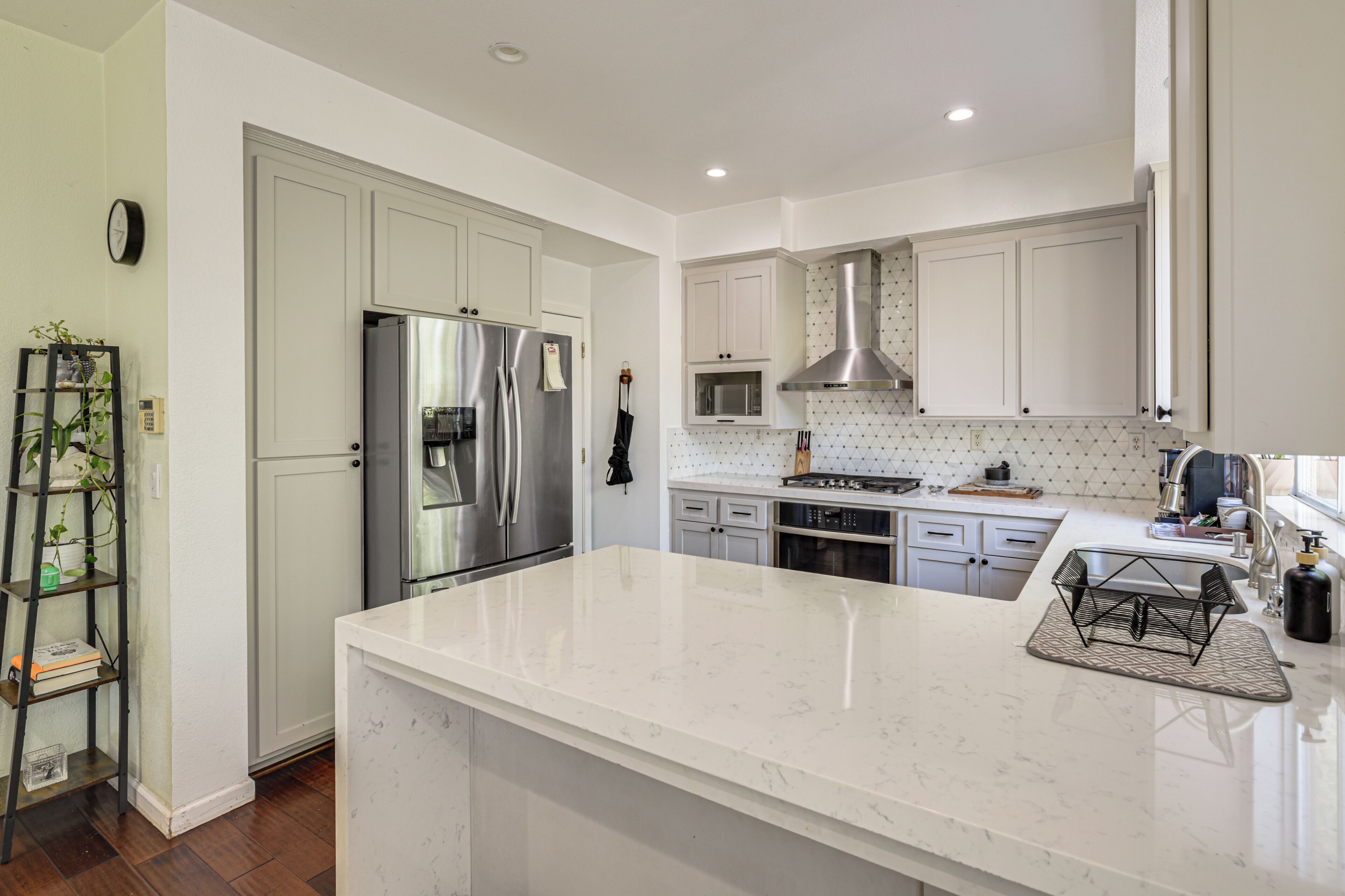 A modern kitchen with white cabinets, stainless steel appliances, and a marble countertop.
