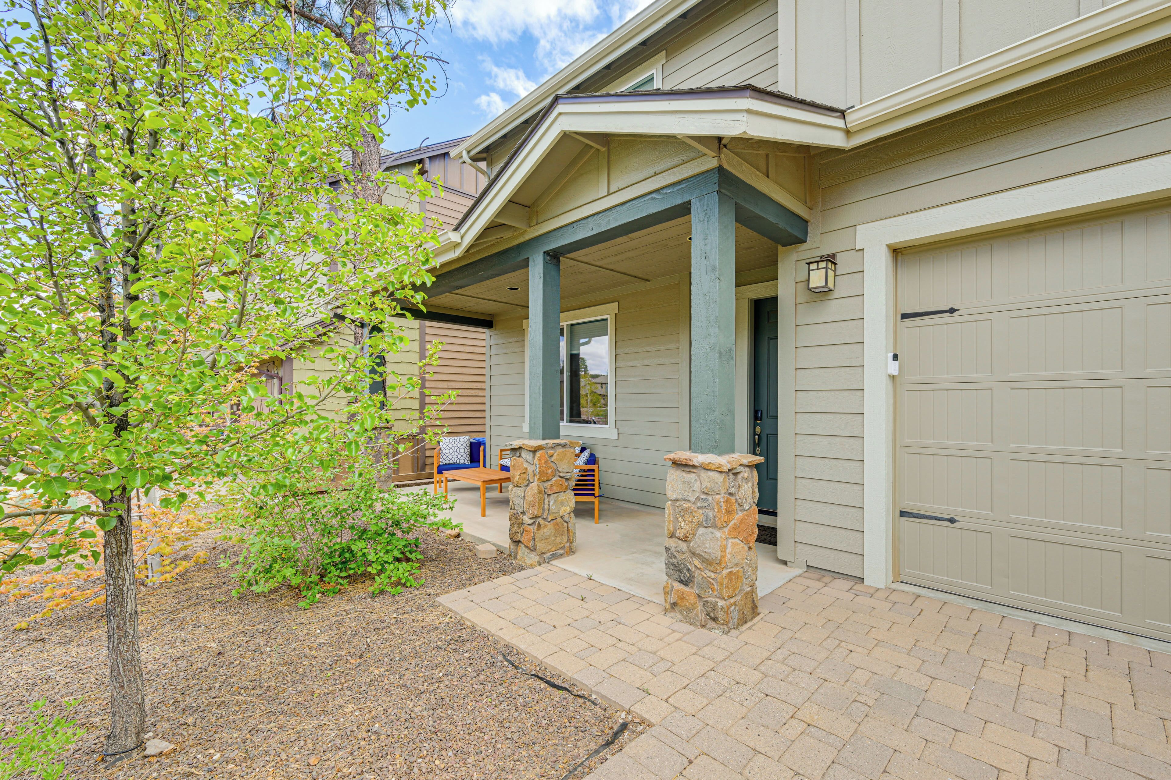 A residential building with a covered porch, stone pillars, a garage door, and a small patio area with outdoor furniture.