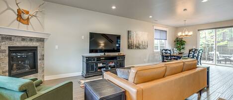 A spacious living room with a fireplace, a large flat-screen TV, a leather sofa, and a dining area with a view.