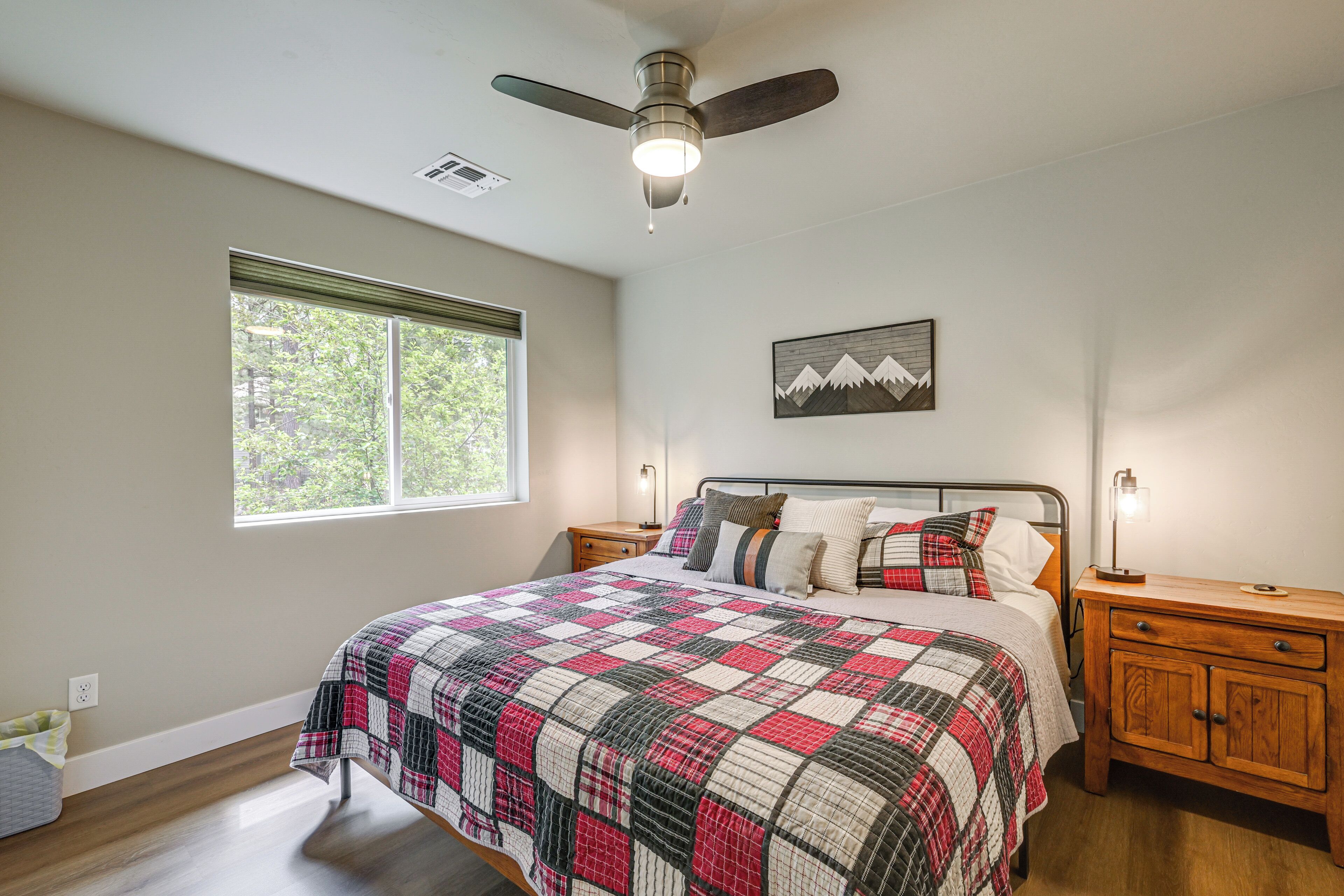 A bedroom with a bed, a ceiling fan, a window, a nightstand, and a wall-mounted lamp.