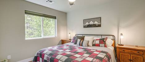 A bedroom with a bed, a ceiling fan, a window, a nightstand, and a wall-mounted lamp.