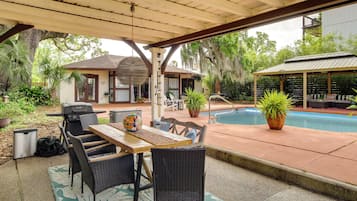 Eine Außenpatio mit Holztisch und -stühlen, einem Grill und einem Pool.