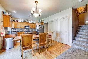 A kitchen with wooden cabinets, a dining table with chairs, a refrigerator, and a microwave. - Suburban Treasure Valley Home w/ Fenced Backyard (Meridian)