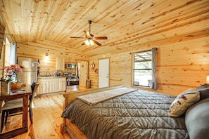 Ein Holzblockhaus-Interieur mit Bett, Esstisch, Küchenzeile und Deckenventilator.