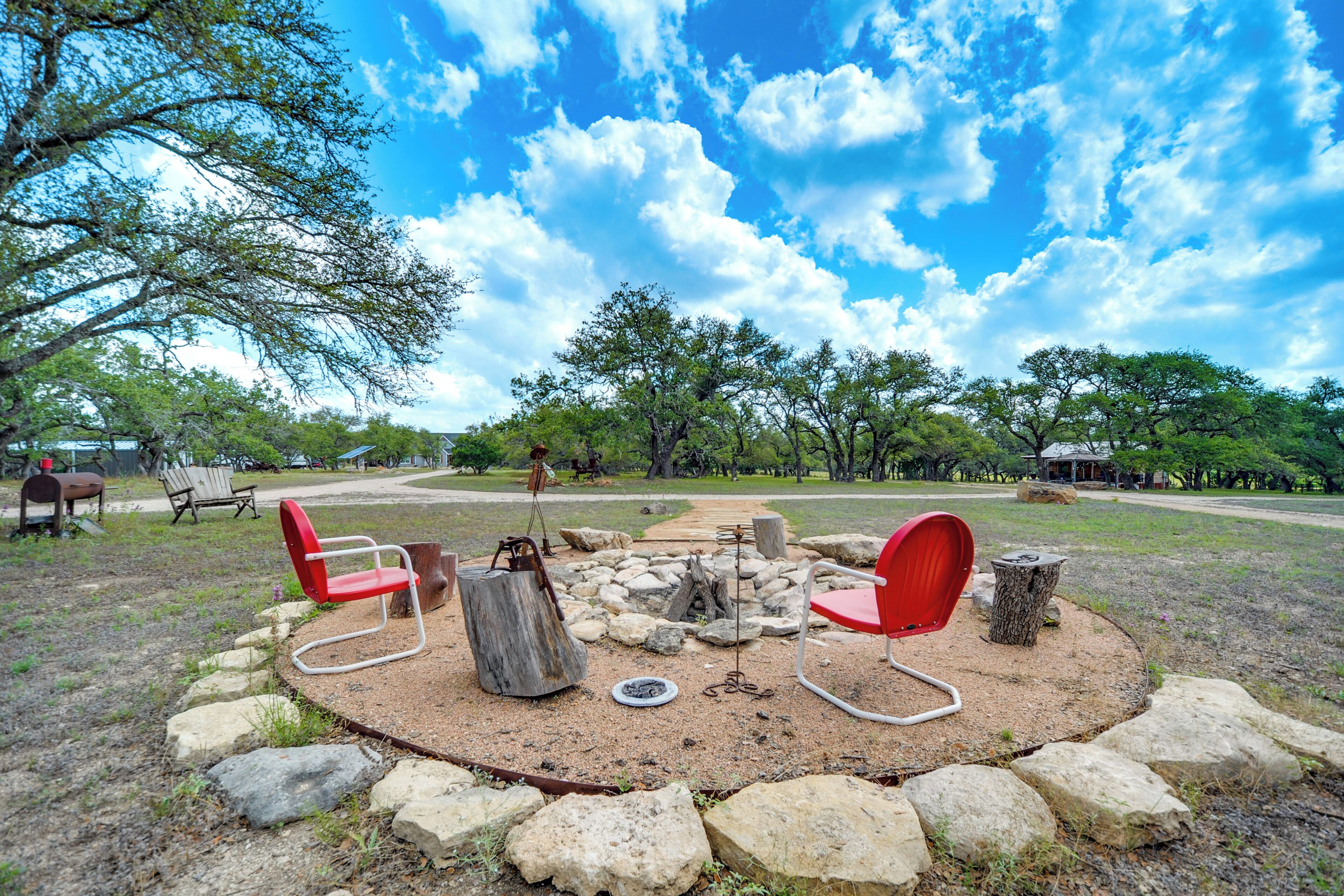 A circular seating area with red chairs and a fire pit, surrounded by rocks and trees, with a clear sky in the background.