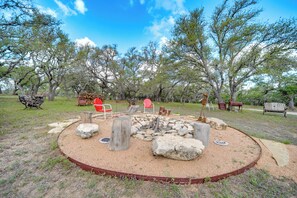 A circular fire pit area with seating, surrounded by trees and a gravel path. - 2 Studio Cabins! Hill Country Escape w/ Fire Pit (Johnson City)