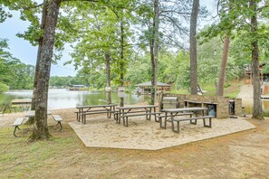 Zona de picnic junto al lago con bancos y una parrilla, rodeada de árboles.
