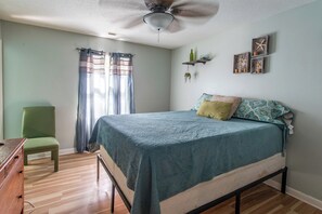Ein Schlafzimmer mit Bett, Sessel, Deckenventilator und Wanddekorationen.