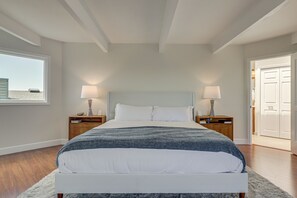 A bedroom with a large bed, two bedside tables with lamps, a window, and a door leading to another room. - Dog-friendly Haven w/ Stunning Views in Bodega Bay (Bodega Bay)