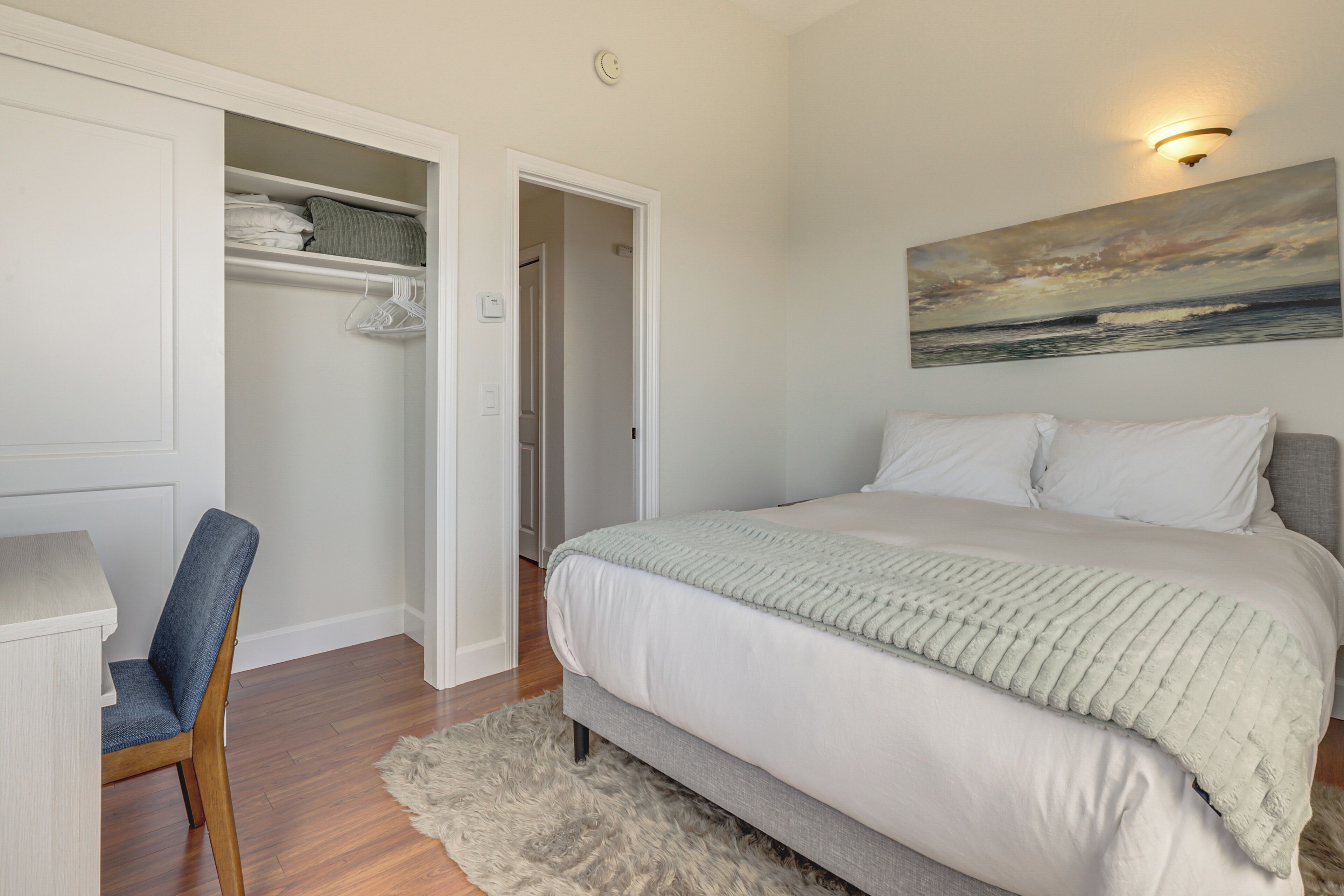 Ein Schlafzimmer mit Bett, Stuhl, Schrank und einem Bild an der Wand.