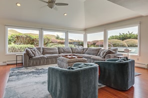 A modern living room with a sectional sofa, two armchairs, a coffee table, and large windows offering a view of landscaped hills. - Dog-friendly Haven w/ Stunning Views in Bodega Bay (Bodega Bay)