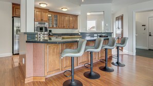 A modern kitchen with wooden cabinets, a central island with bar stools, stainless steel appliances, and a large window. - Dog-friendly Haven w/ Stunning Views in Bodega Bay (Bodega Bay)