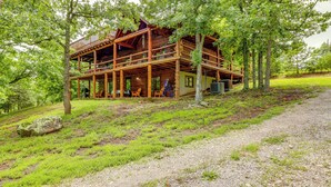 A rustic cabin with a wooden deck and multiple levels, surrounded by lush greenery. - Game Room + Roof Deck: Ozarks Group Getaway! (Harrison)