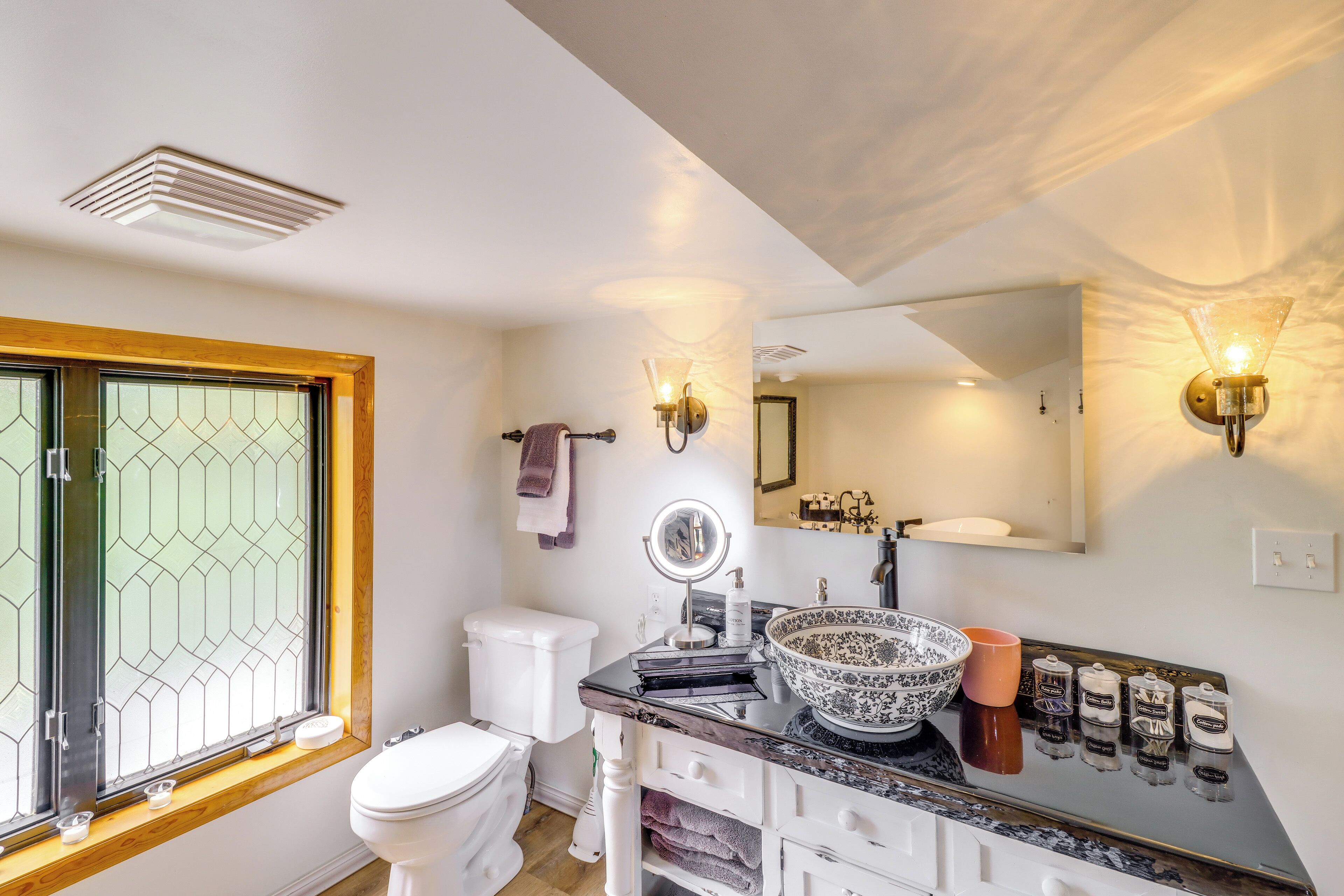 A bathroom with a toilet, sink, mirror, and window with a geometric pattern.