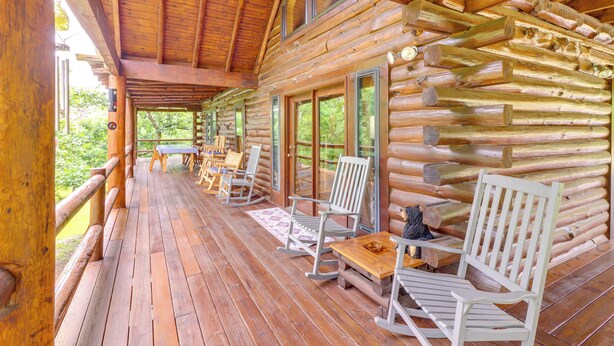 A log cabin with a wooden deck, rocking chairs, and a table. - Game Room + Roof Deck: Ozarks Group Getaway! (Harrison)