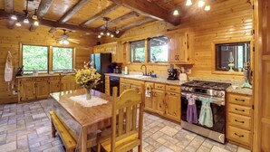 A wooden cabin kitchen with a dining table, wooden chairs, a stove, and a sink. - Game Room + Roof Deck: Ozarks Group Getaway! (Harrison)