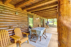 A log cabin with a covered porch, wooden chairs, a table, and a view of the outdoors.