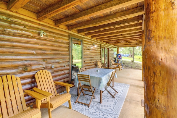 Eine Blockhütte mit überdachter Veranda, Holzstühlen, einem Tisch und Blick ins Freie.