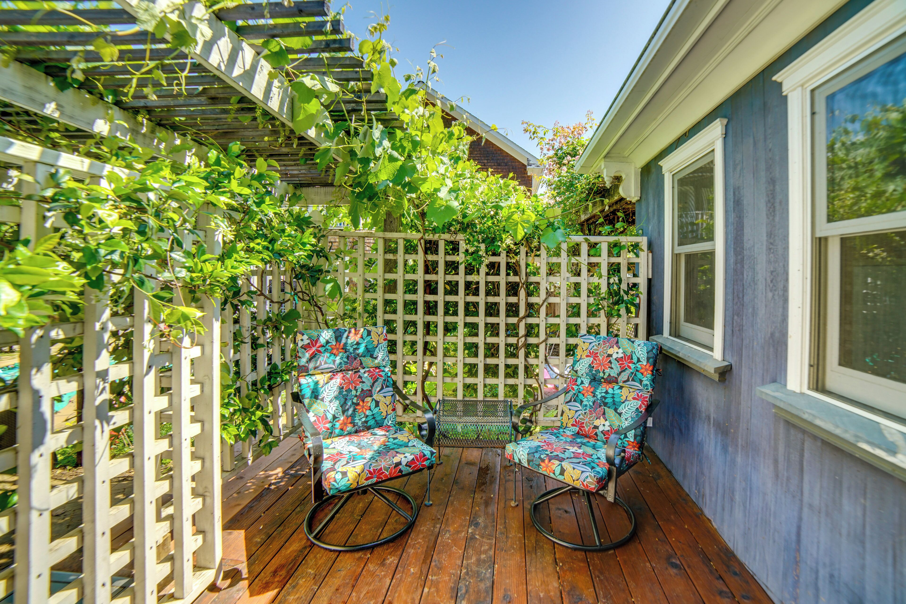Une terrasse en bois avec deux fauteuils à bascule, une clôture blanche en treillis et un bâtiment bleu en arrière-plan.