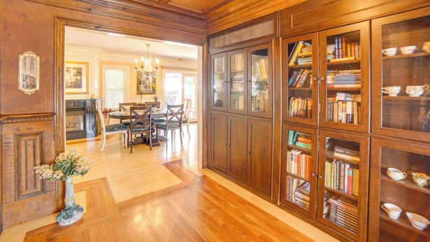 Een ruime kamer met houten vloeren, een eethoek met een kroonluchter en een grote boekenkast vol boeken.
