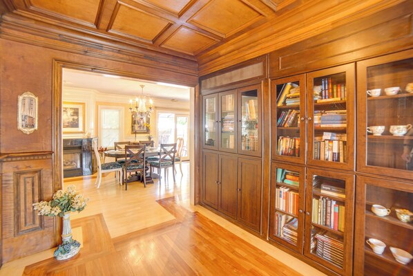 Una habitación amplia con piso de madera, un comedor con candelabro y una gran estantería llena de libros.
