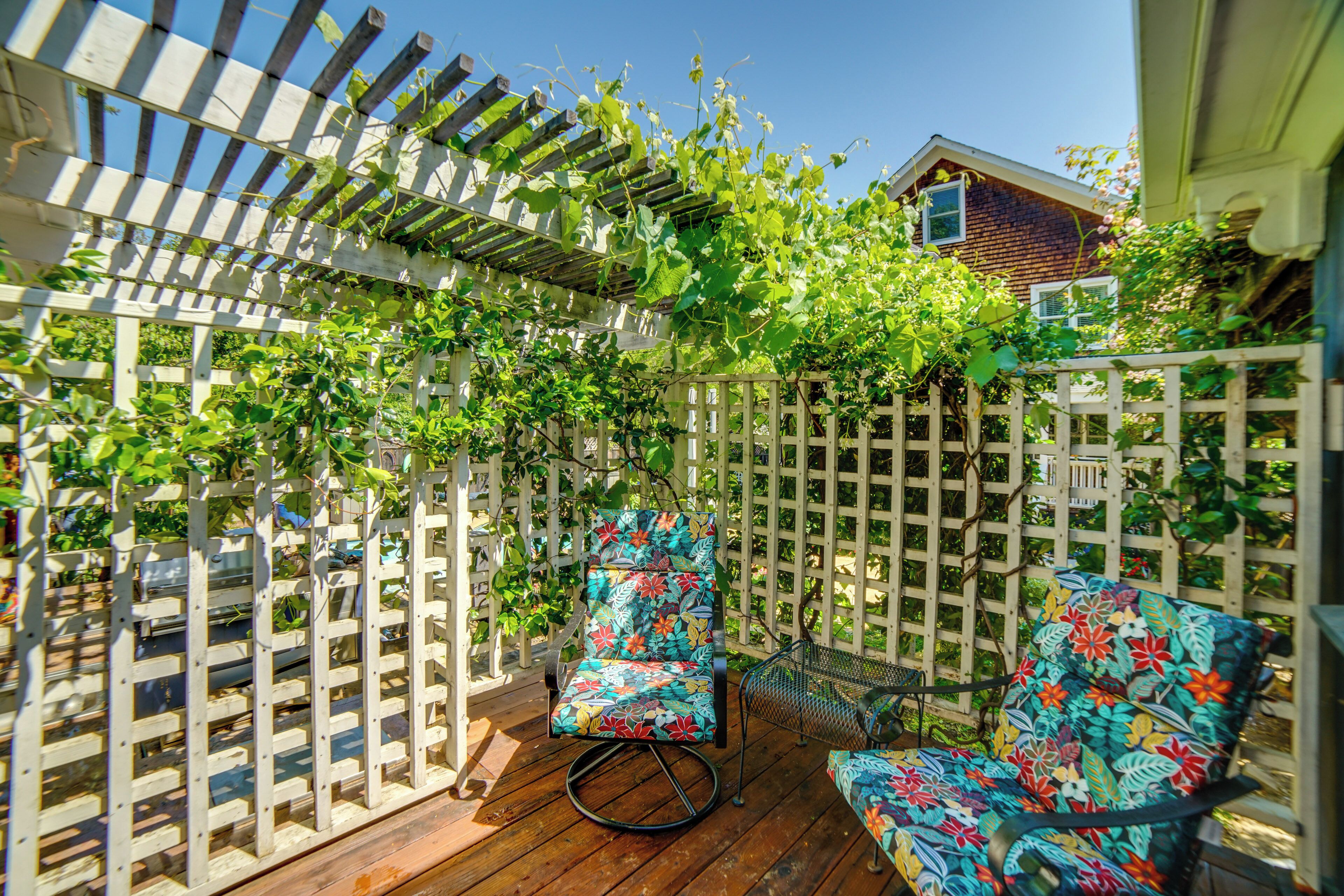 A wooden deck with a white lattice fence, two colorful chairs, and a house in the background.