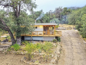 A cabin with a deck, surrounded by trees and a stone wall.