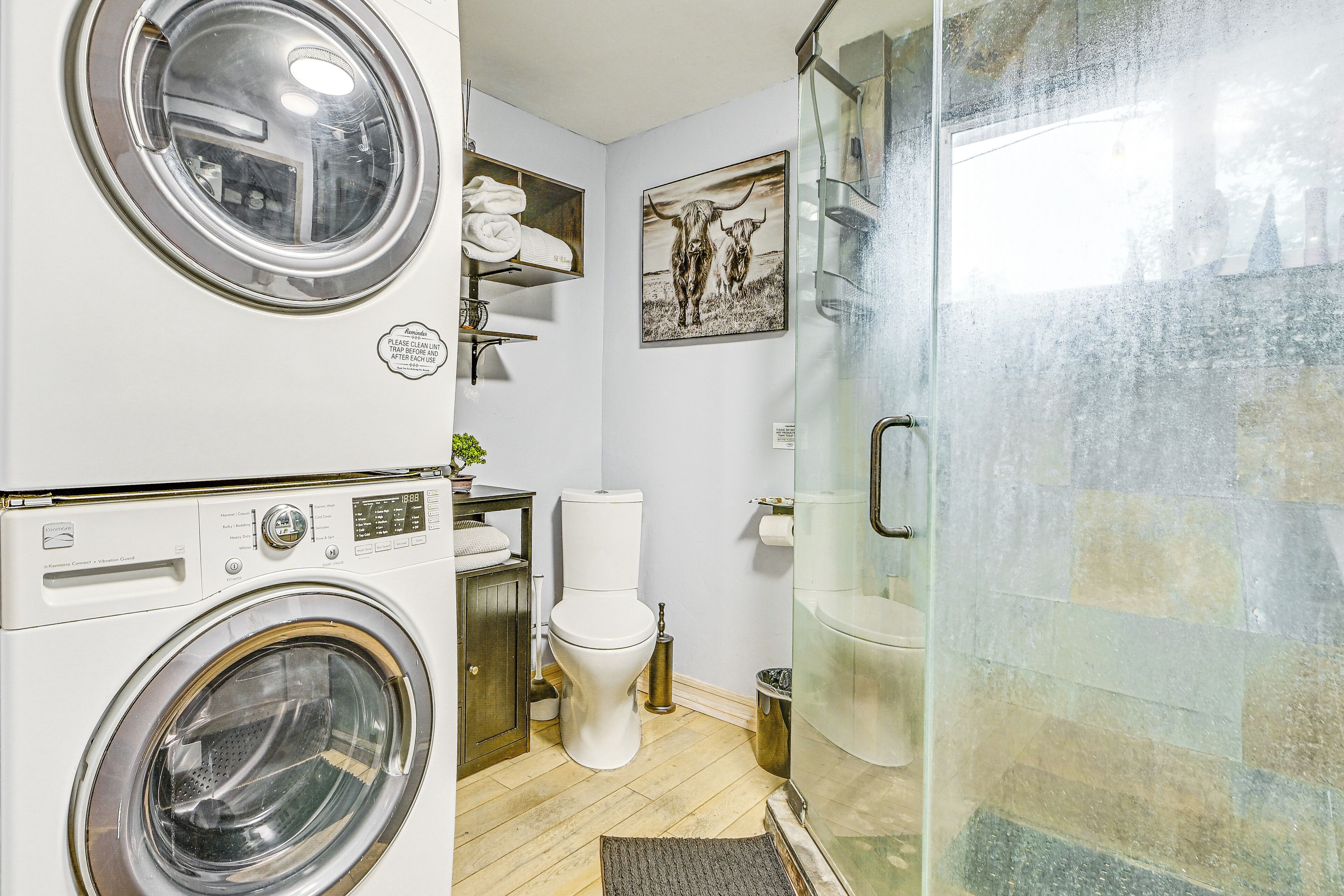 A compact bathroom with a washing machine, toilet, and glass shower enclosure.