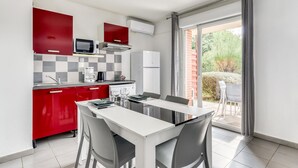 A modern kitchen with red cabinets, a white countertop, and a dining area with a table and chairs. - Family Studio Near Argeles Beaches (Argelès-sur-Mer)