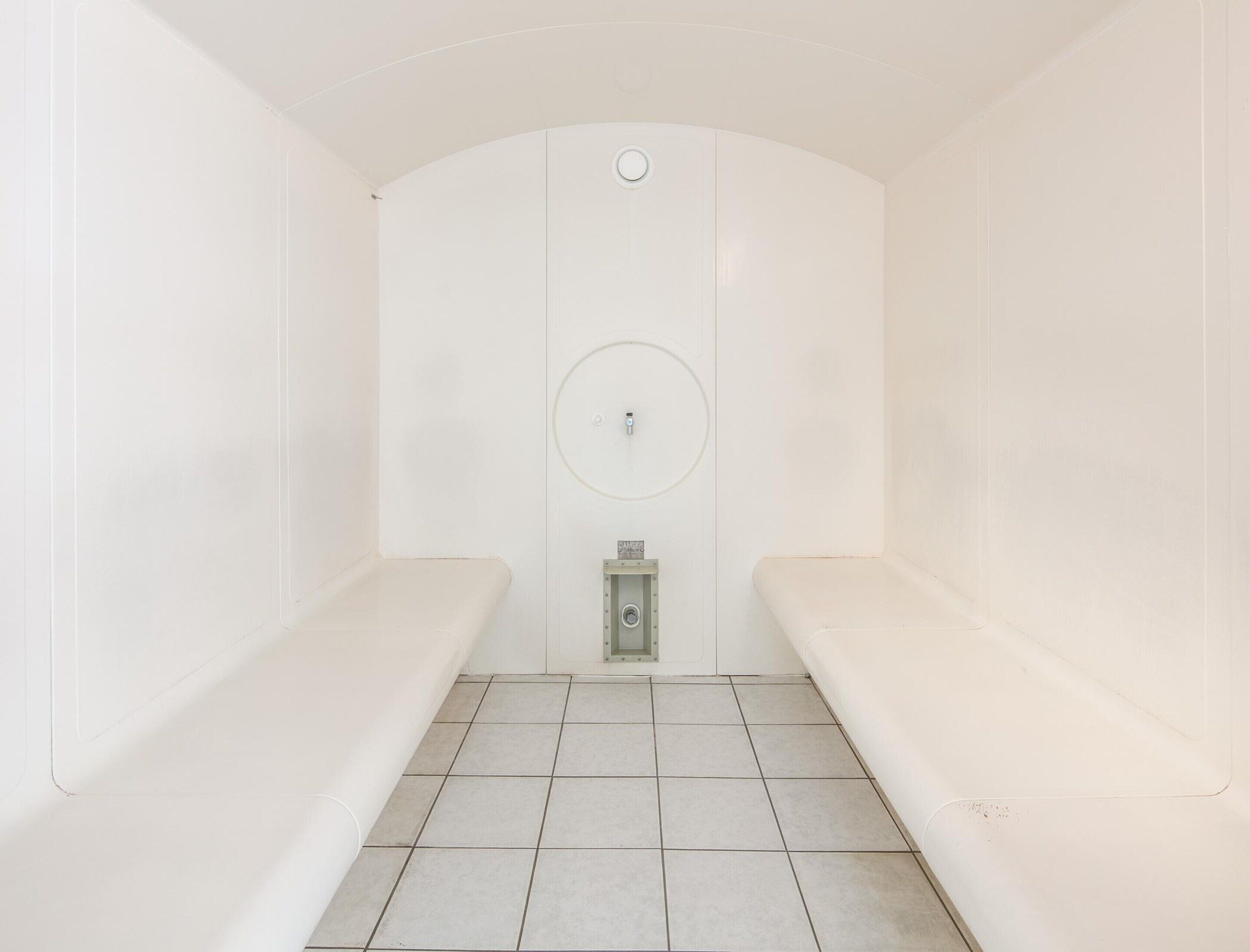 A small, white, enclosed space with a bench, a circular sink, and a small cabinet.