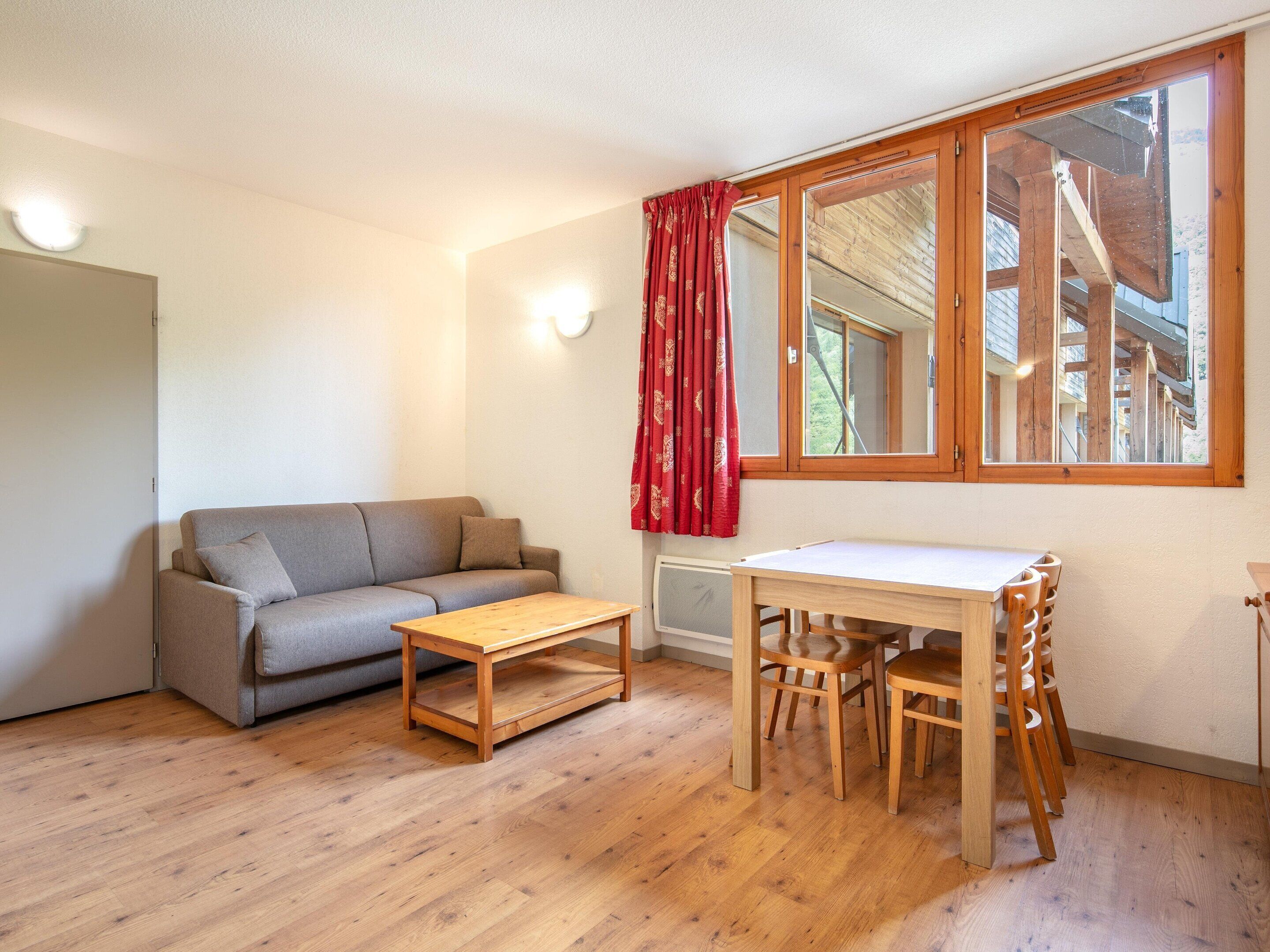 A room with a sofa, a wooden table, and a window with a view of a building.