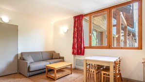 Een kamer met een bank, een houten tafel en een raam met uitzicht op een gebouw.