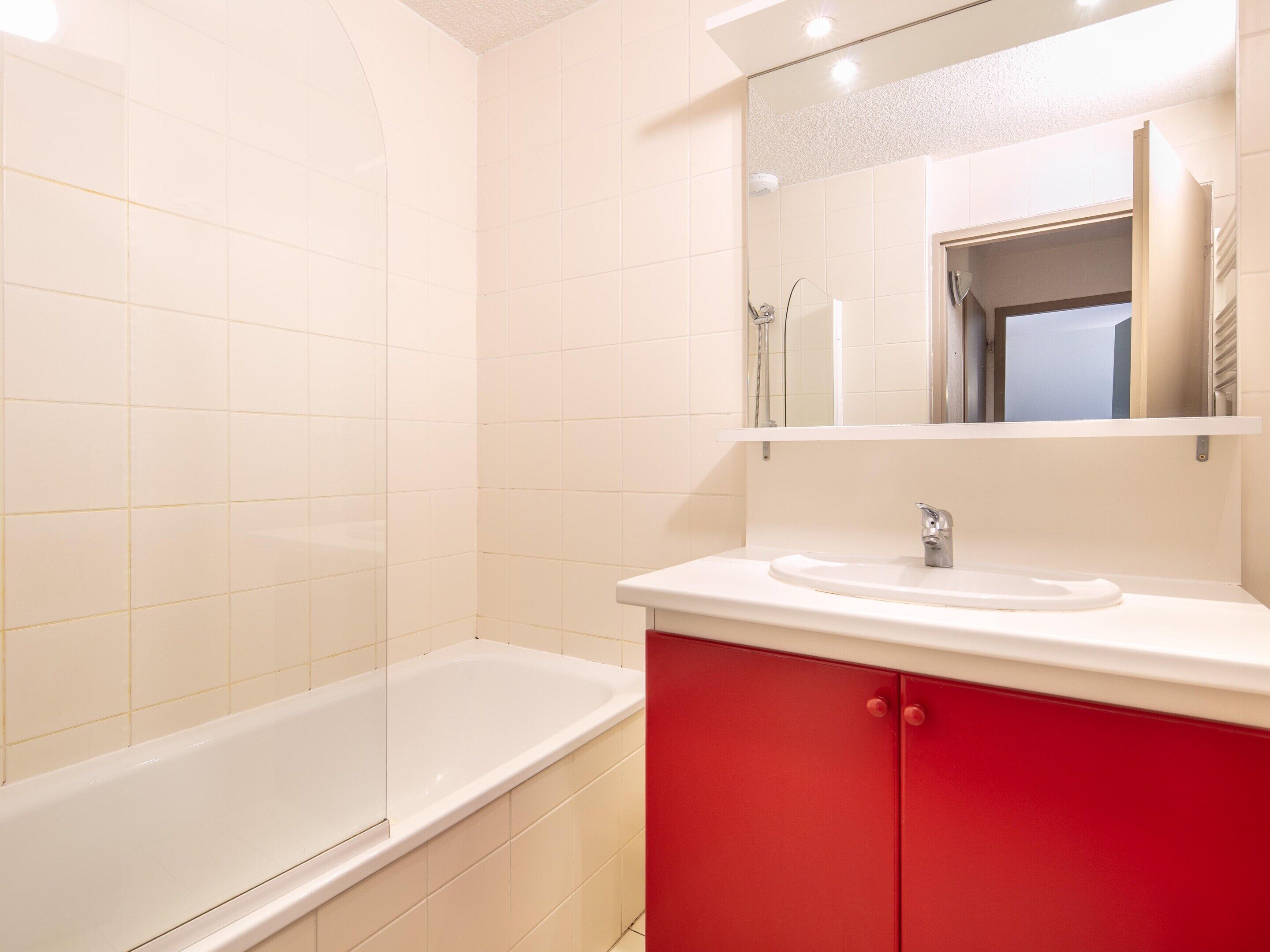 Ein Badezimmer mit einer weißen Badewanne, einem roten Waschtisch und einem Spiegel über dem Waschbecken.