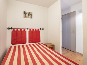 Ein Schlafzimmer mit gestreifter Bettdecke, einem kleinen Nachttisch, einer Tür und einem an der Wand hängenden Bild.