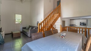 Ampla sala de estar com uma cama grande, escada de madeira, área de cozinha e uma pequena janela.