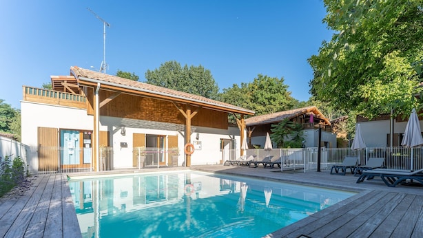 Piscina com deck de madeira, área de estar coberta e um edifício com telhado telhado.