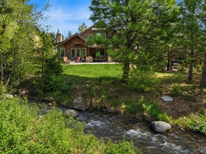 Eine Lodge mit Terrasse, einem Bach und umliegender Bepflanzung.