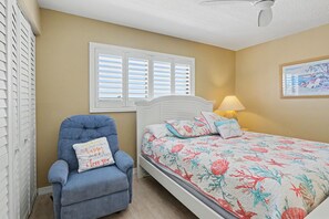 Une chambre à coucher avec un lit, une chaise, une fenêtre avec des stores, une lampe et un tableau au mur.