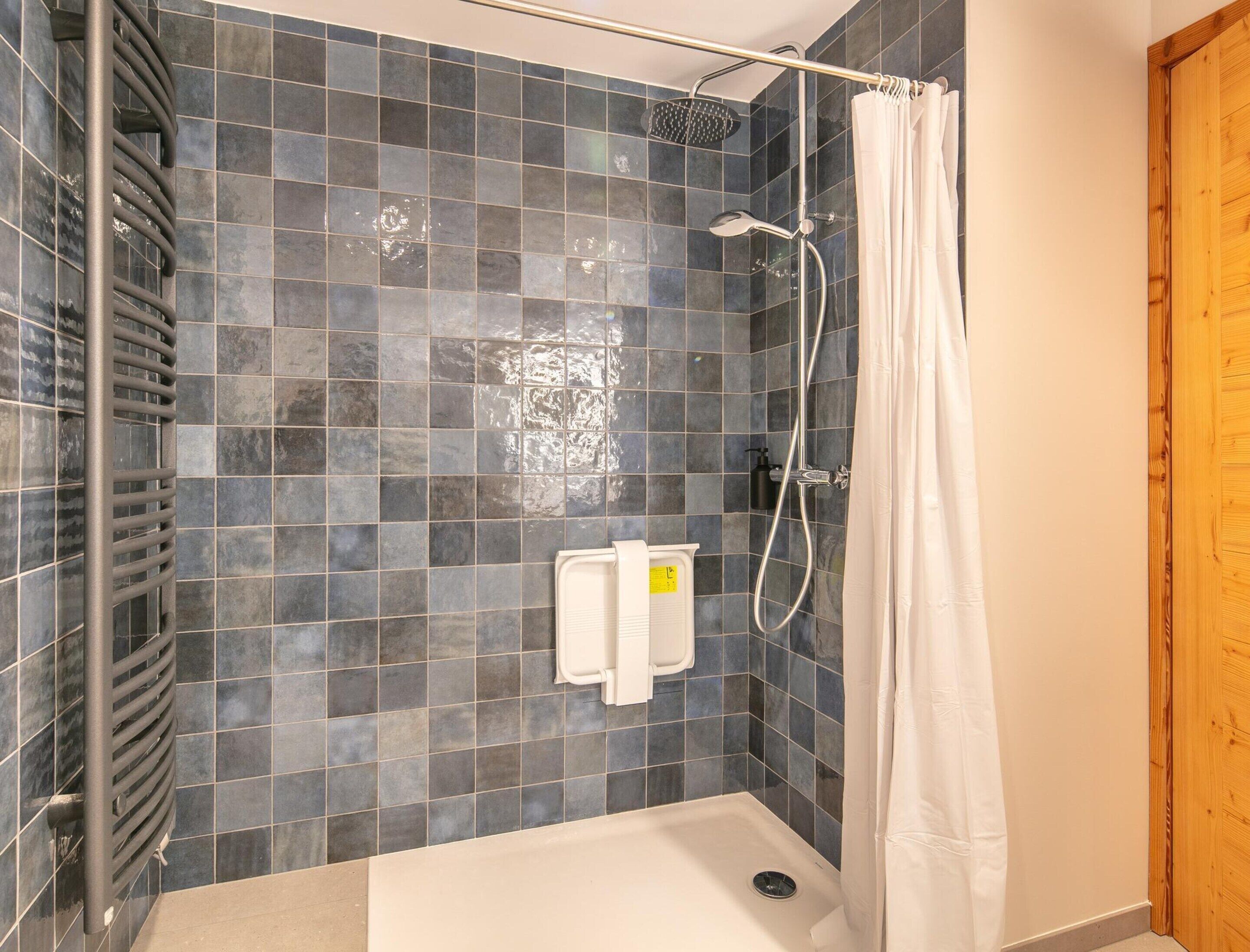 A shower area with a tiled wall, a showerhead, a handheld shower attachment, and a white towel dispenser.