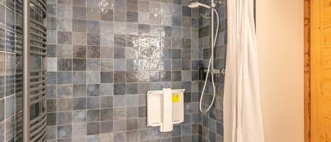 A shower area with a tiled wall, a showerhead, a handheld shower attachment, and a white towel dispenser.