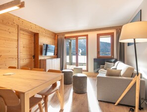 Ein Holzinterieur mit Esstisch, Sofa, Fernseher und großen Fenstern.