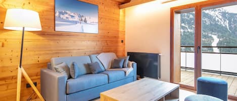 Una habitación acogedora con techo de madera, un sofá, una mesa de centro, una lámpara y un televisor.