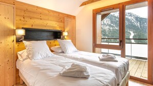 A bedroom with two beds, wooden headboard, bedside lamps, and a large window with a mountain view. - 6-person Apartment Near Ski Lifts (Vaujany)