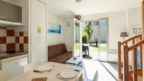 Une pièce comprenant une table à manger, des chaises, un canapé, un coin cuisine et donnant sur l’extérieur.
