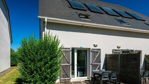 Une maison avec une terrasse, un patio avec des chaises, une clôture en bois et un petit arbre.